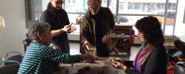 Four individuals gathered around a card table shaping clay with their hands.